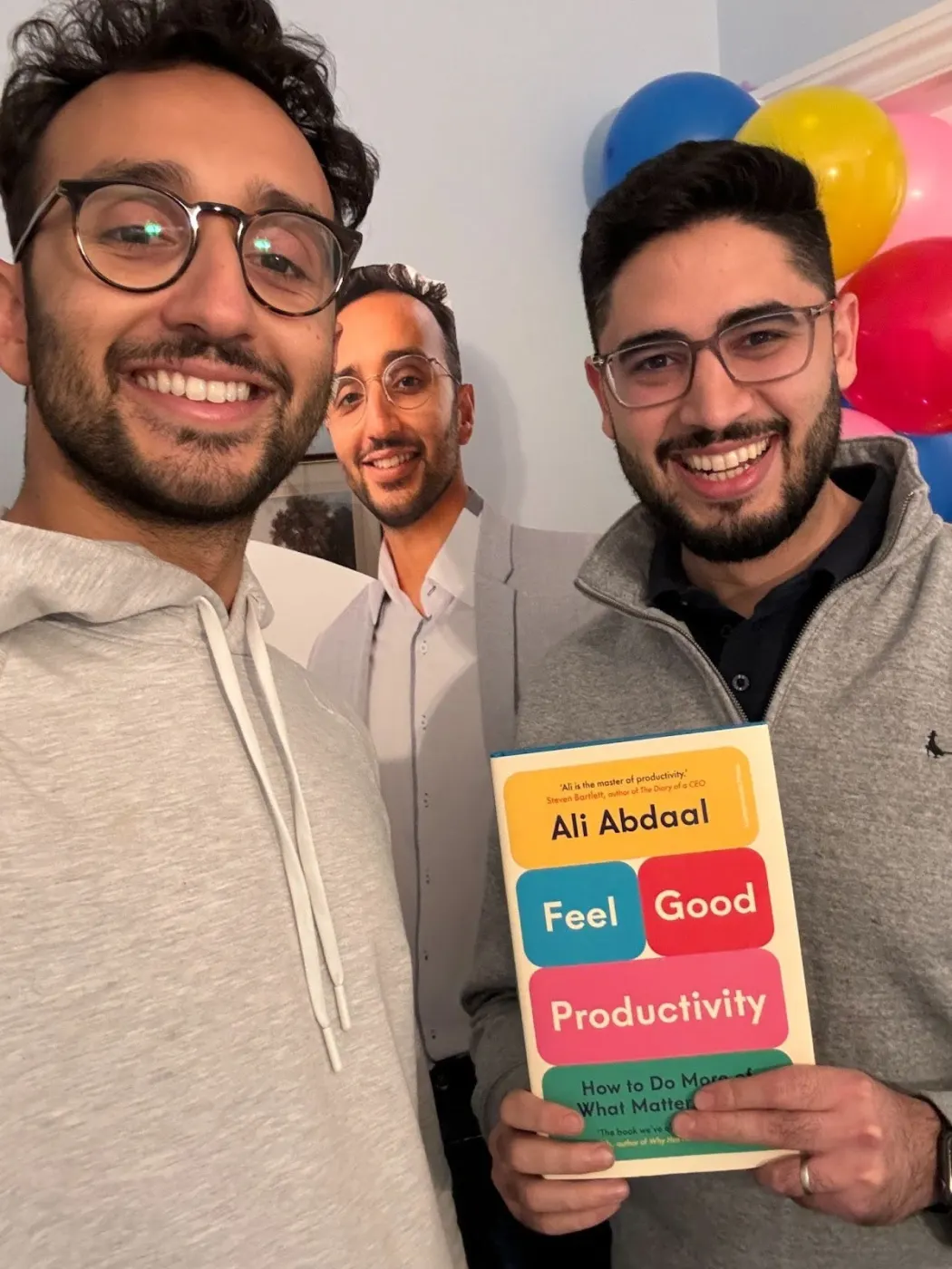 Ali with two friends, one holding a copy of Feel-Good Productivity