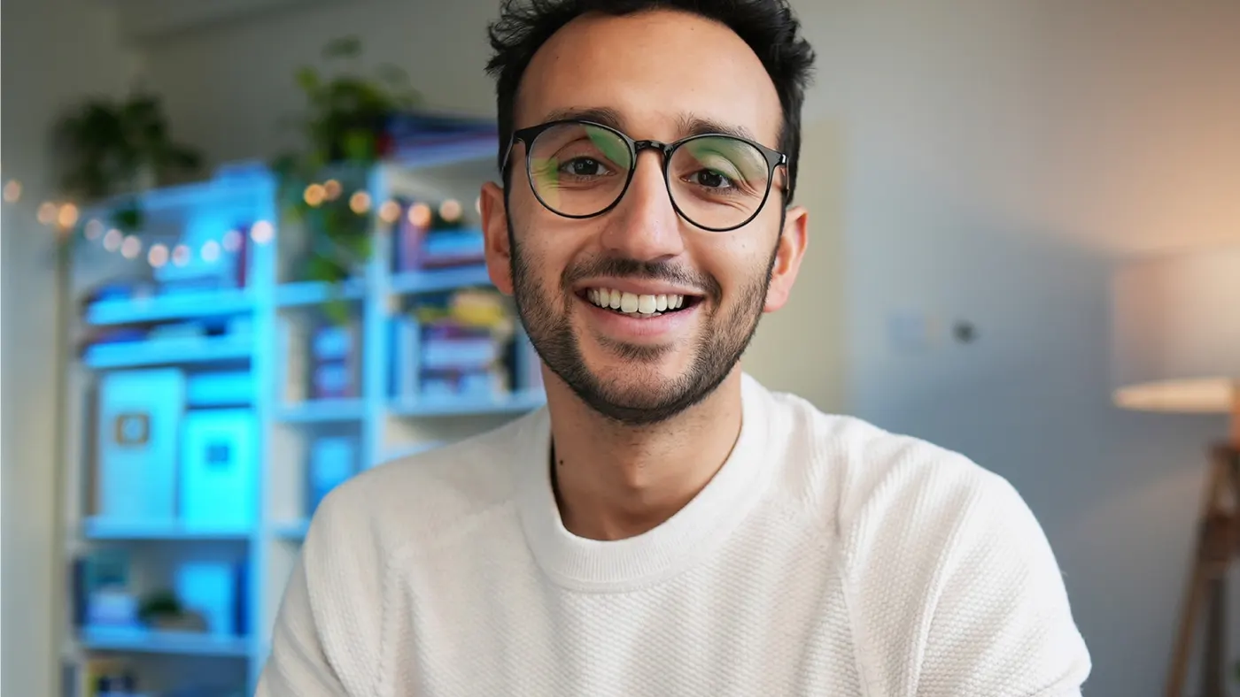 Ali smiling at his desk in a studio lit with blue shelves