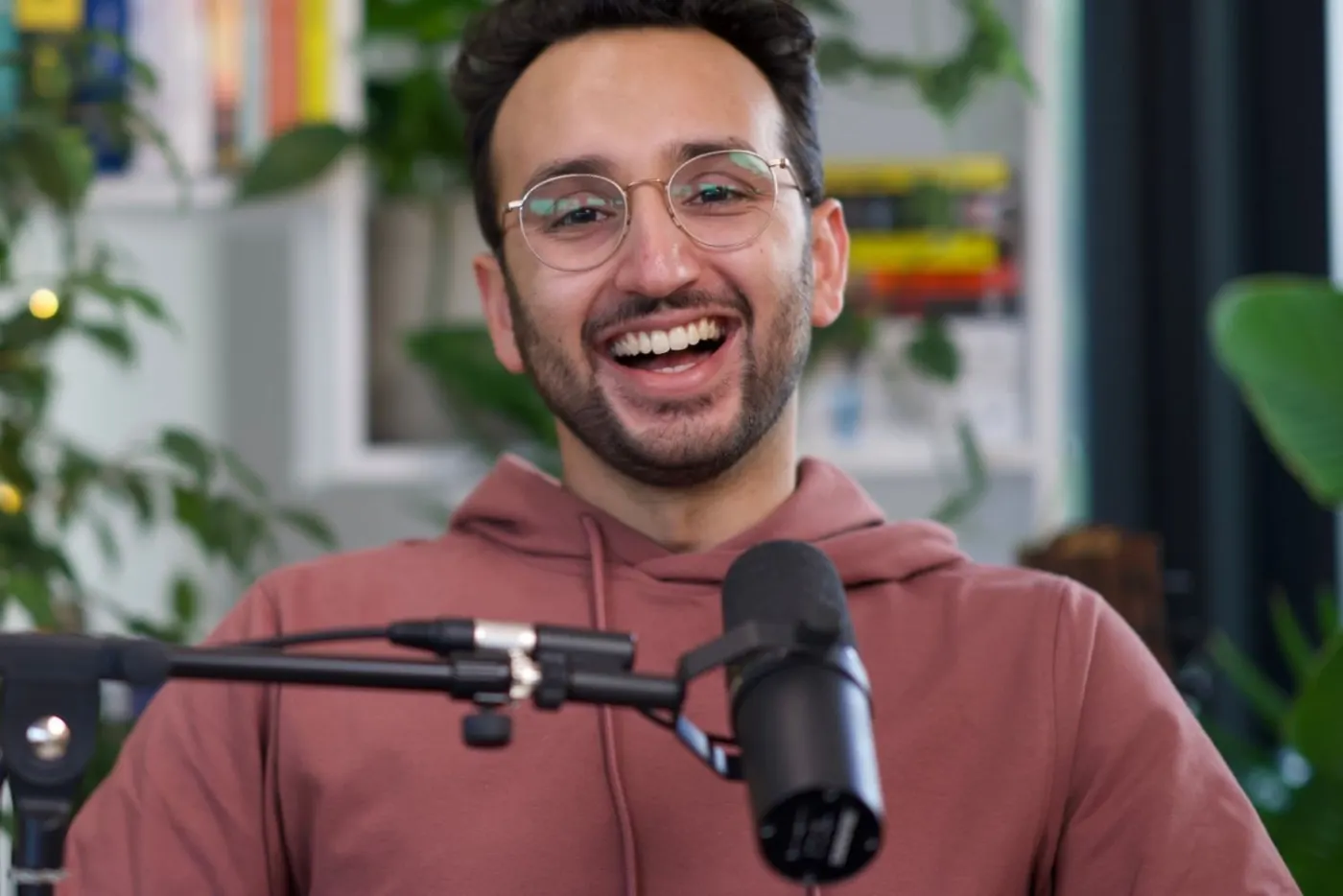 Ali laughing at a podcast microphone in a red hoodie