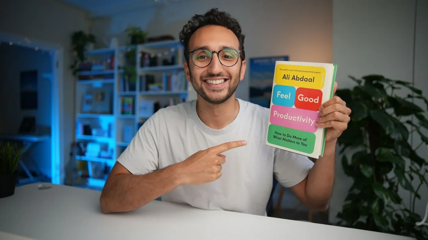 Ali in a white T-shirt pointing at his book in his home studio