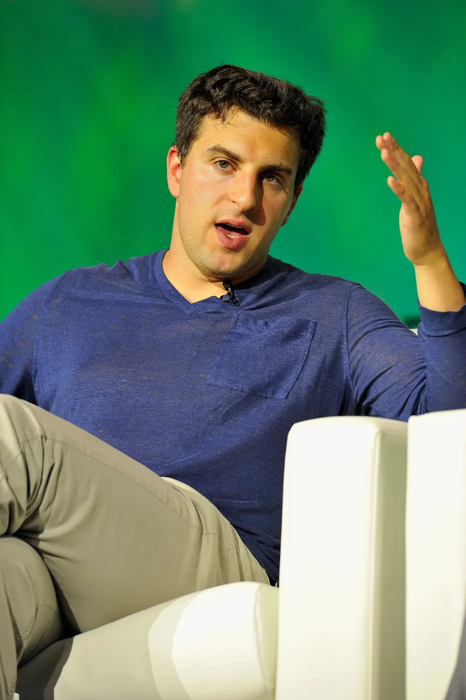Chesky on stage in white chair, navy shirt, green backdrop