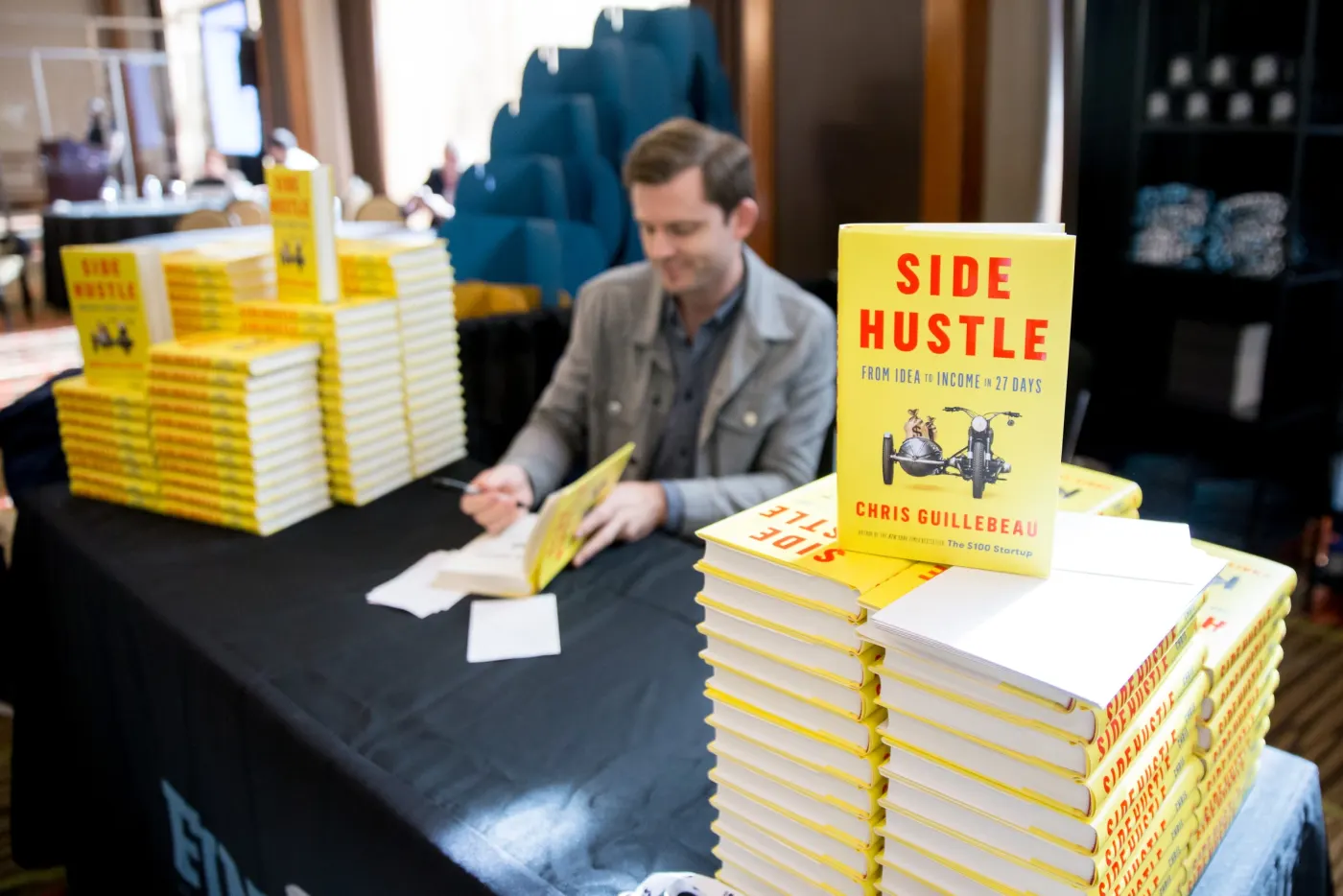 Guillebeau signing yellow Side Hustle books at a conference table