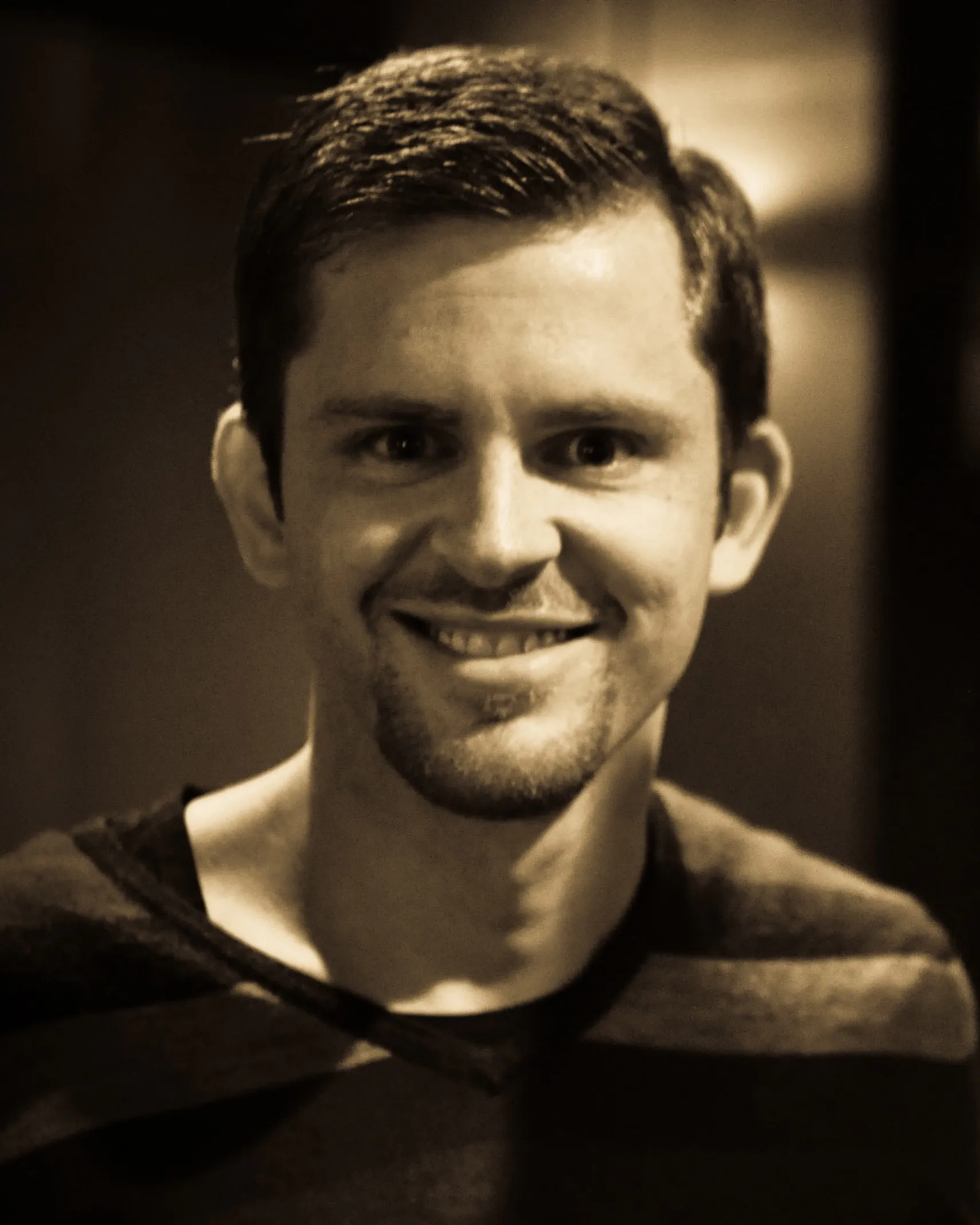 Sepia smiling headshot, striped V-neck, goatee