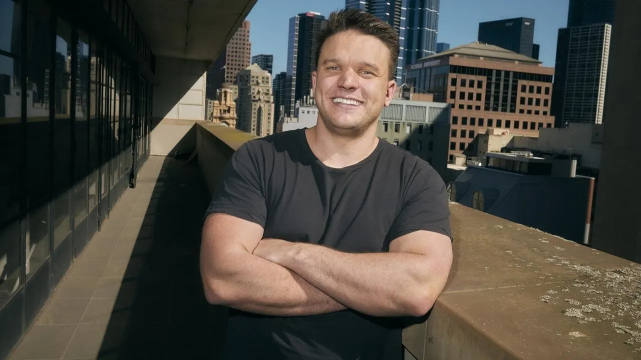 Smiling Craven on Melbourne balcony with Victoria University building behind