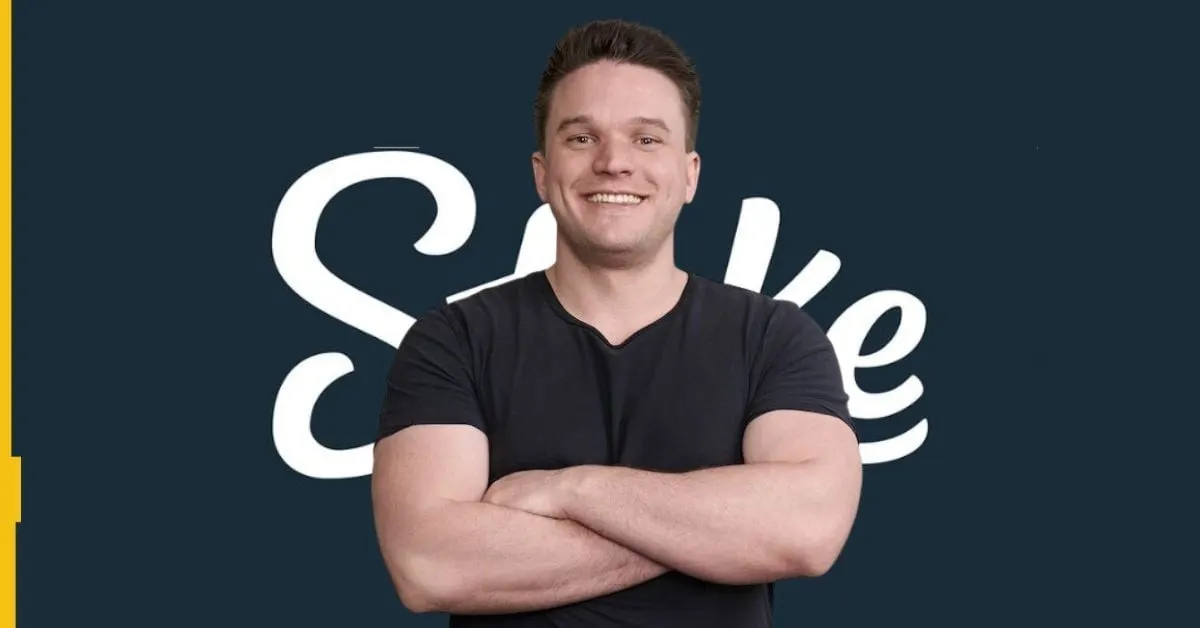 Ed Craven smiling with arms crossed in front of large white Stake logo