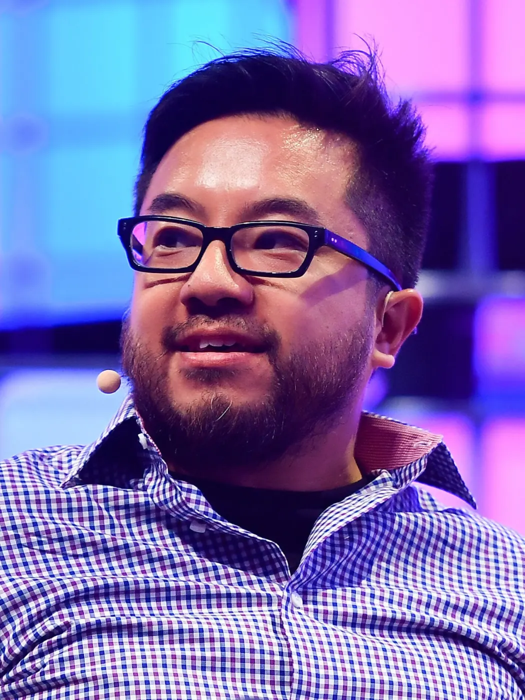Stage portrait of Garry Tan with headset mic, blue-purple LED panels
