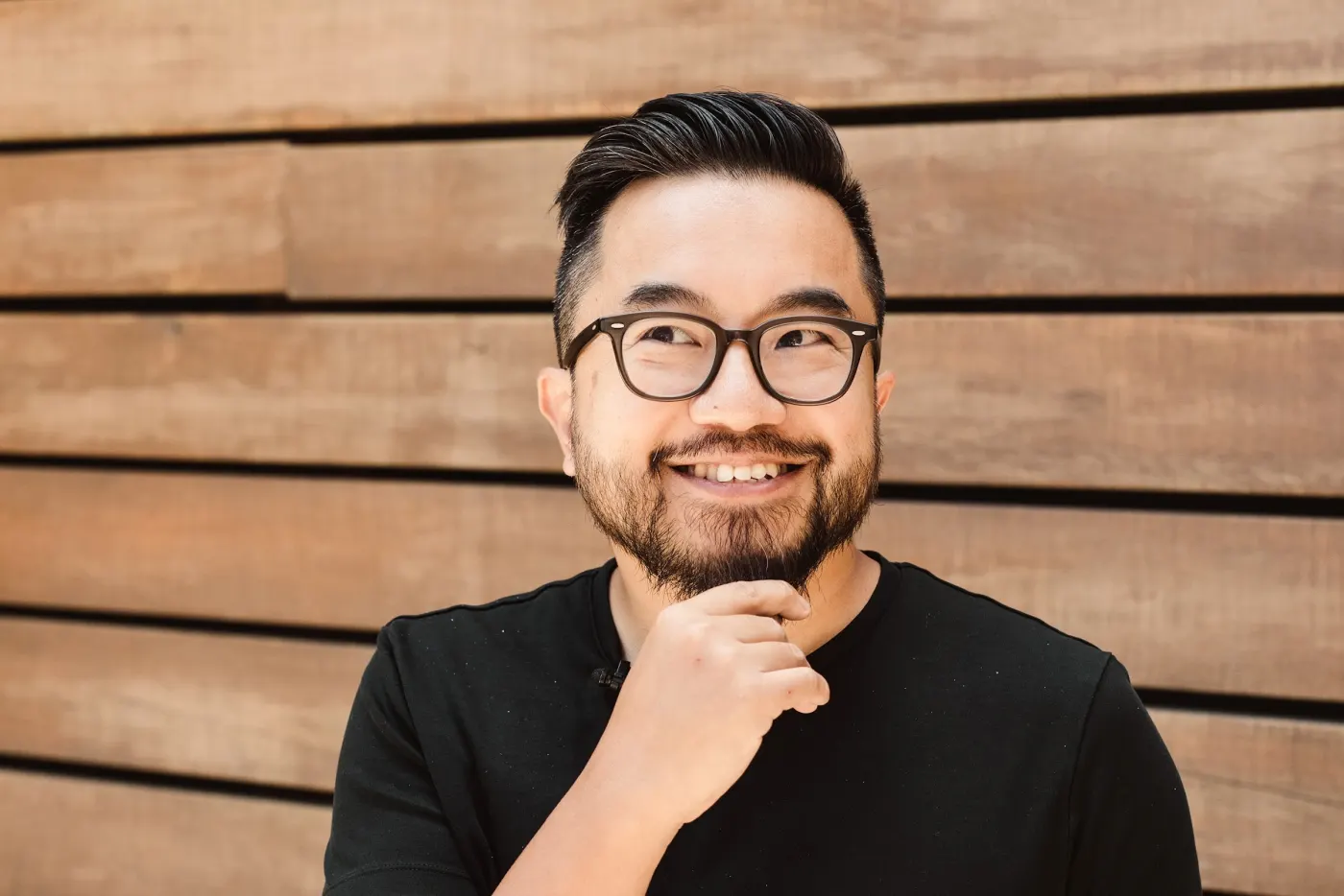 Color portrait of Garry Tan in black tee, hand to chin, wood-plank background