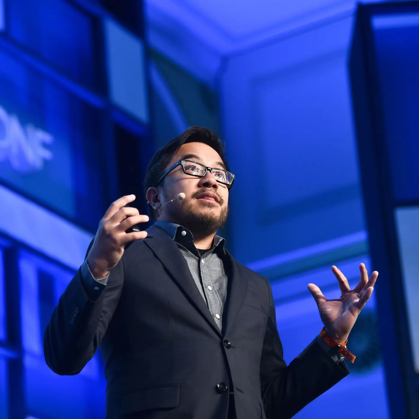 Garry Tan on blue MoneyConf-style stage in blazer, gesturing with headset mic