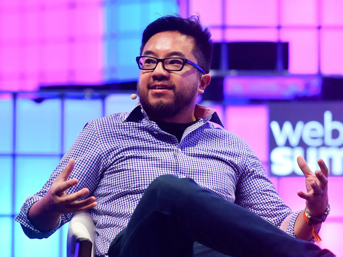 Garry Tan seated speaking at Web Summit with pink-blue cube wall