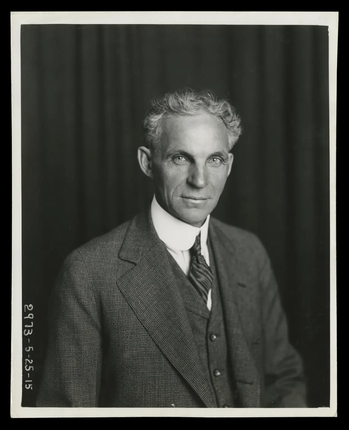 Henry Ford in a dark suit against a dark curtain