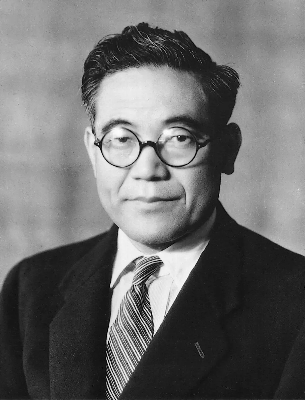 Black-and-white studio portrait of Kiichiro Toyoda in round glasses and a striped tie