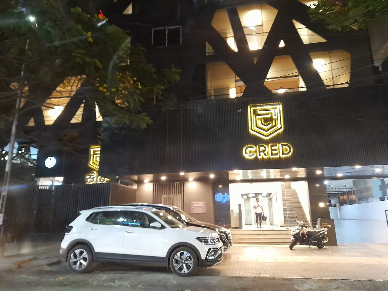 Night exterior of CRED office with glowing gold neon shield logo