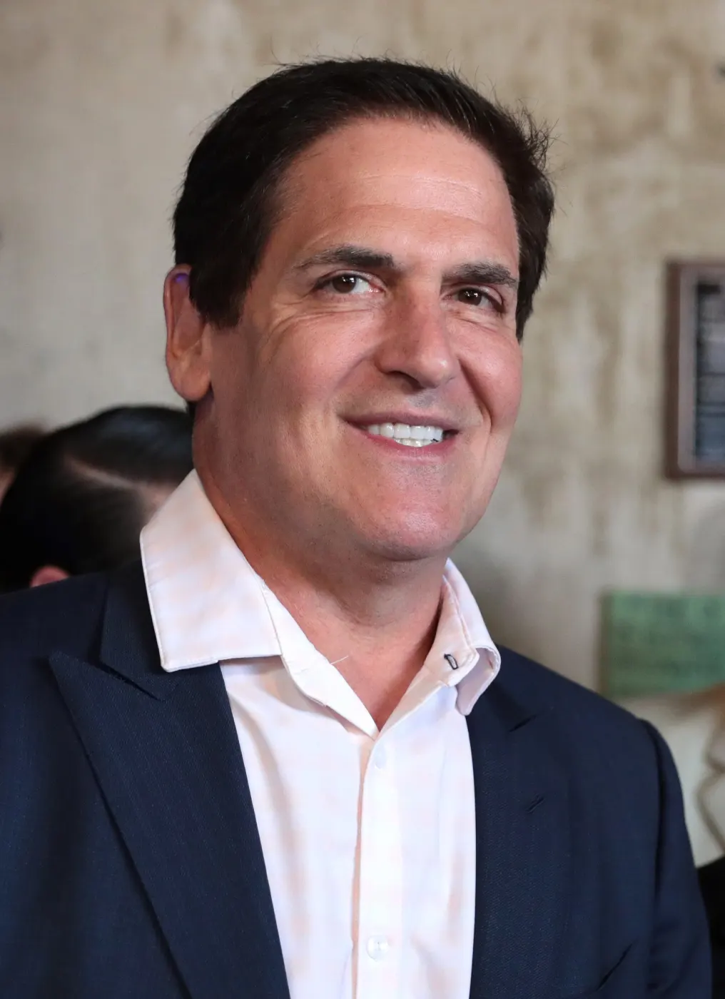 Smiling portrait of Mark Cuban in a white shirt and dark blazer