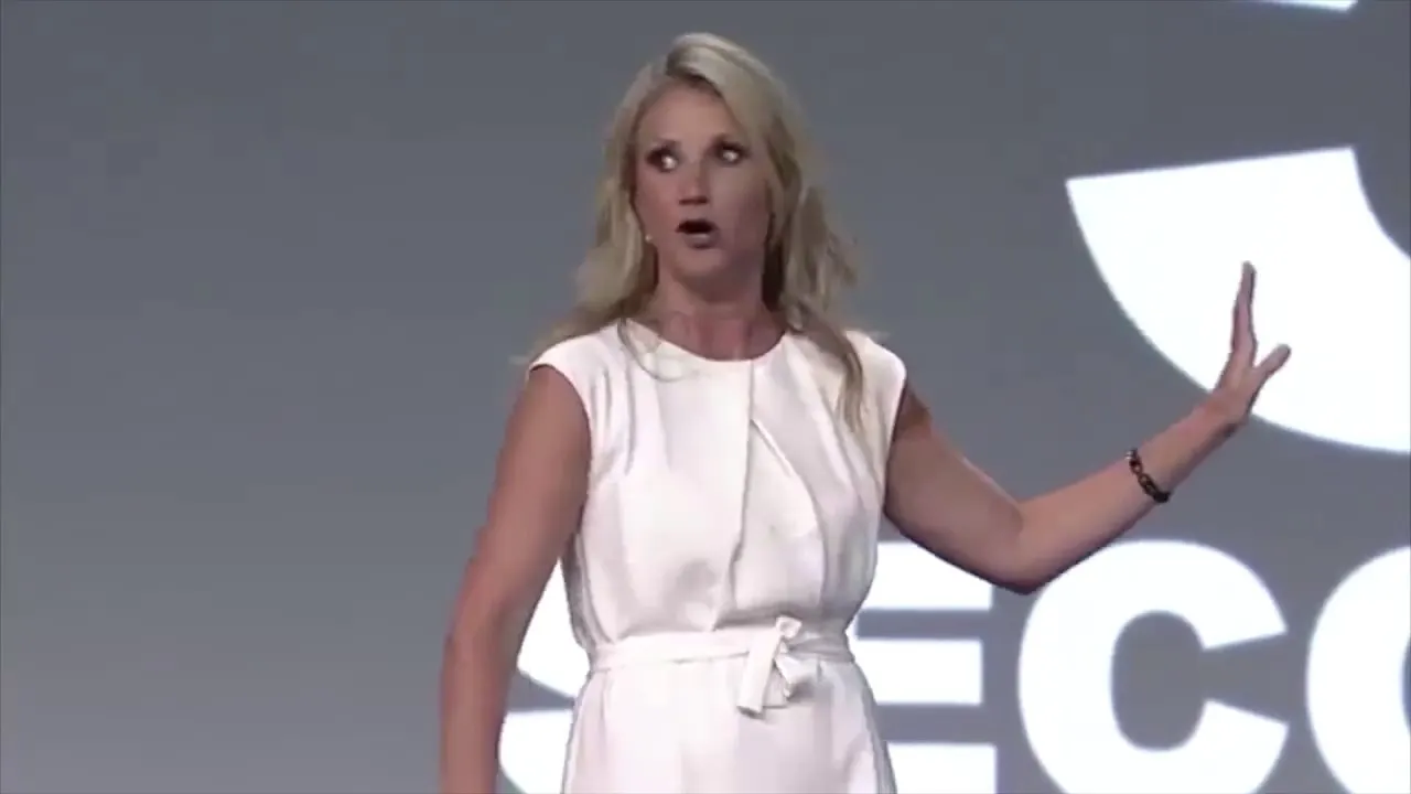 Mel Robbins in a white sleeveless dress gesturing on a stage in front of a large screen