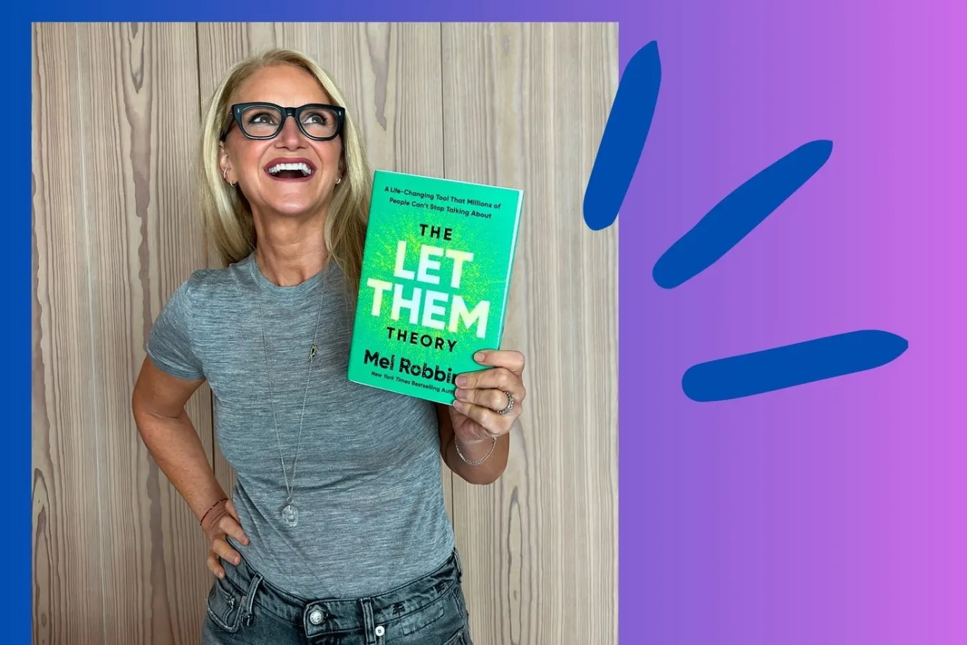 Mel Robbins smiling in a gray T-shirt, holding up a copy of The Let Them Theory