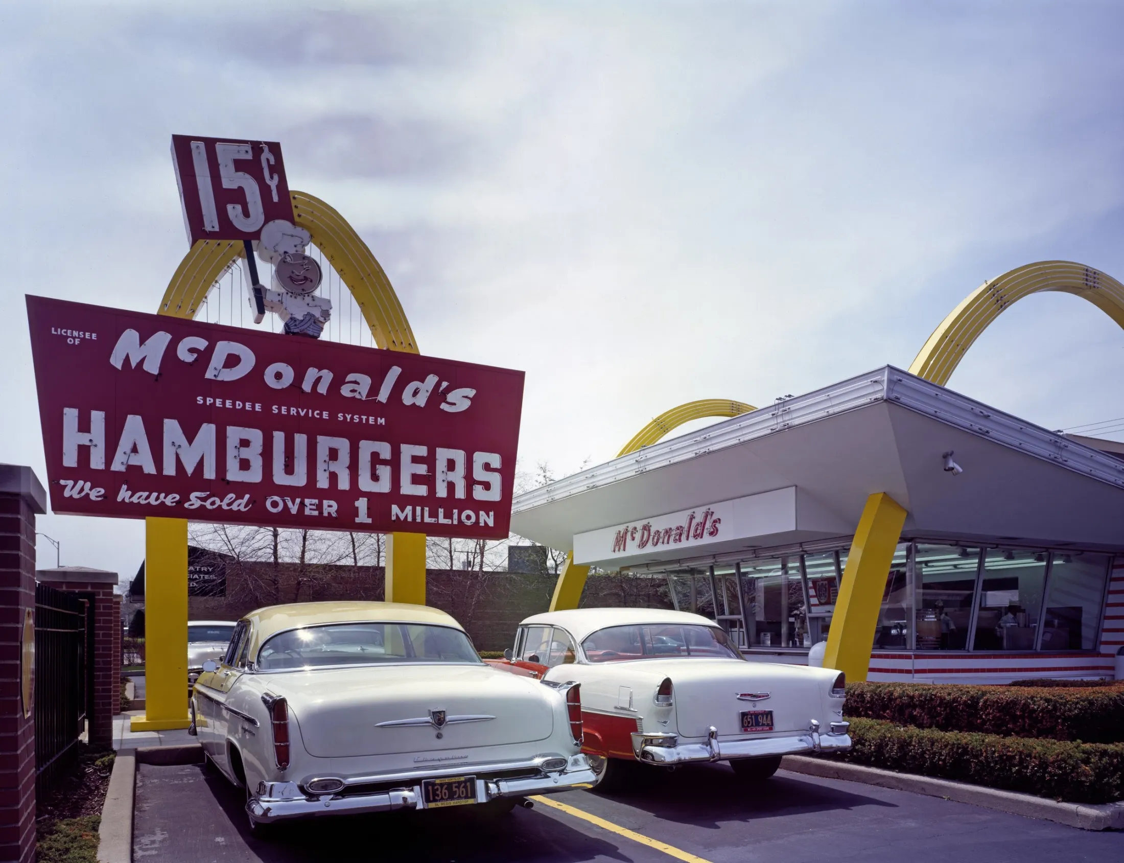 Early-style McDonald's restaurant with golden arches, a red Hamburgers sign, and 1950s cars