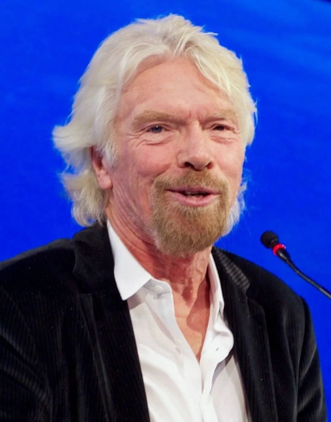 Richard Branson portrait against blue backdrop with microphone