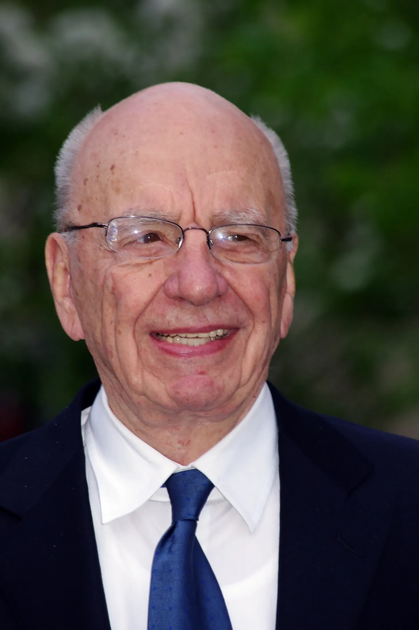 Smiling close portrait, blue tie, green trees behind