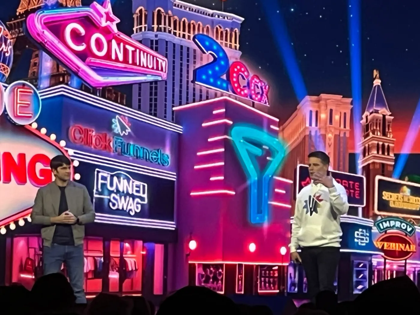 Two men on a neon-lit Las Vegas-style stage set at a Funnel Hacking Live event