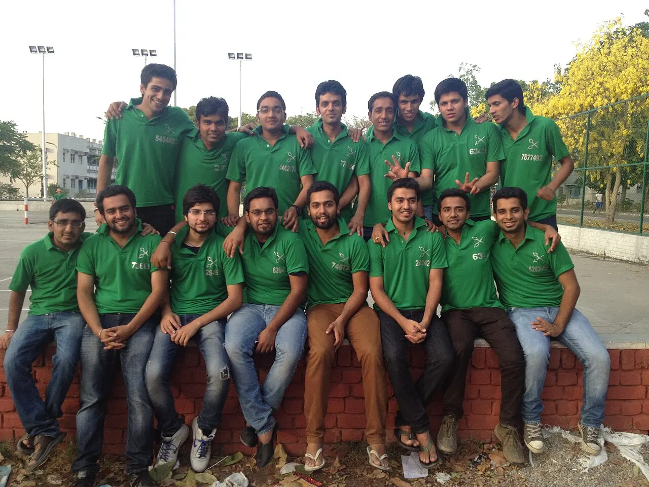 Green-shirt hostel group photo from college years, young faces on a brick ledge