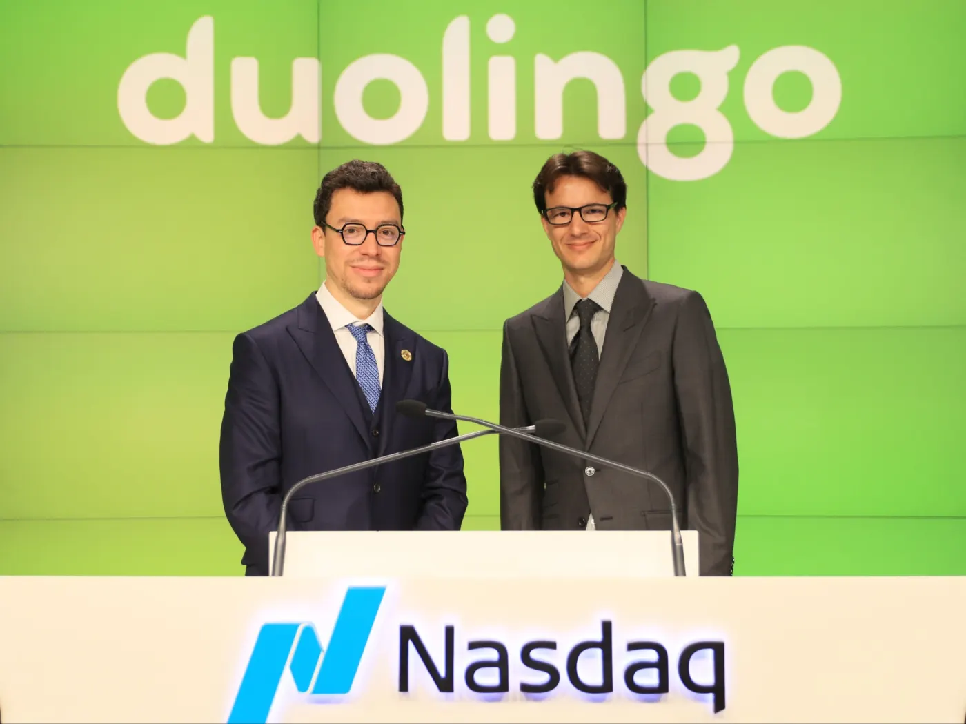 Duolingo leaders in suits on the stage at the Nasdaq, with a large Duolingo sign behind them