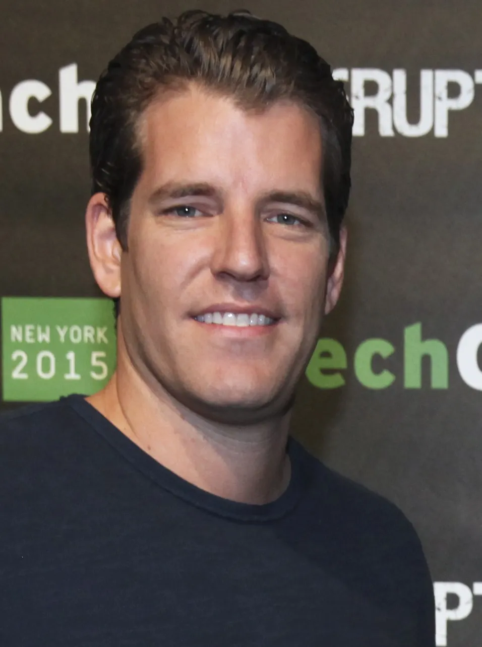 Close portrait of Tyler Winklevoss smiling in front of a TechCrunch Disrupt 2015 backdrop