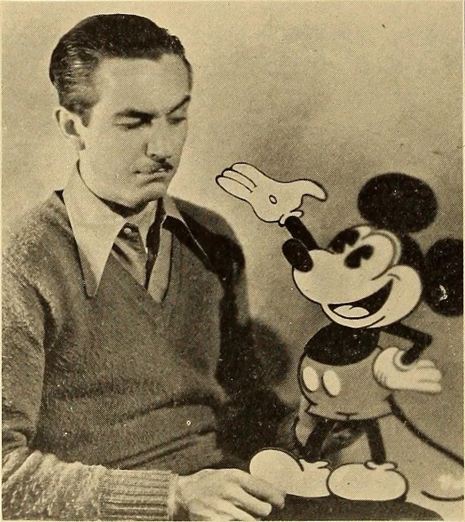 Walt in a sweater beside a drawn Mickey