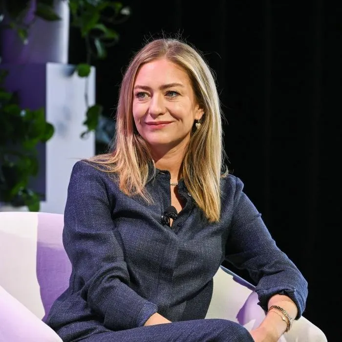 Seated on a conference stage in a denim-blue suit
