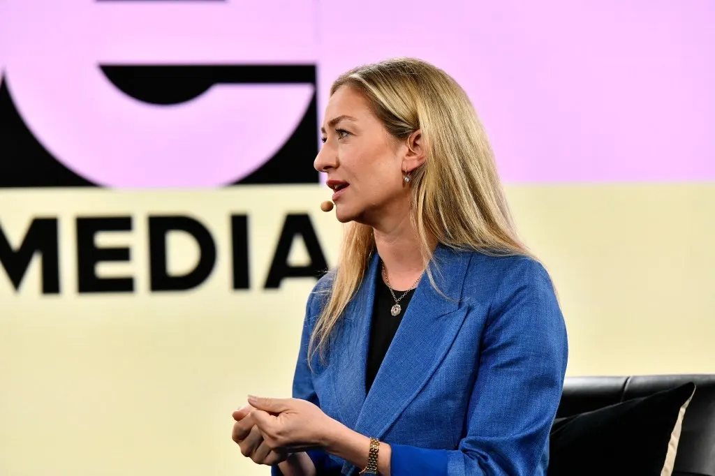 Speaking on a media stage in a blue blazer