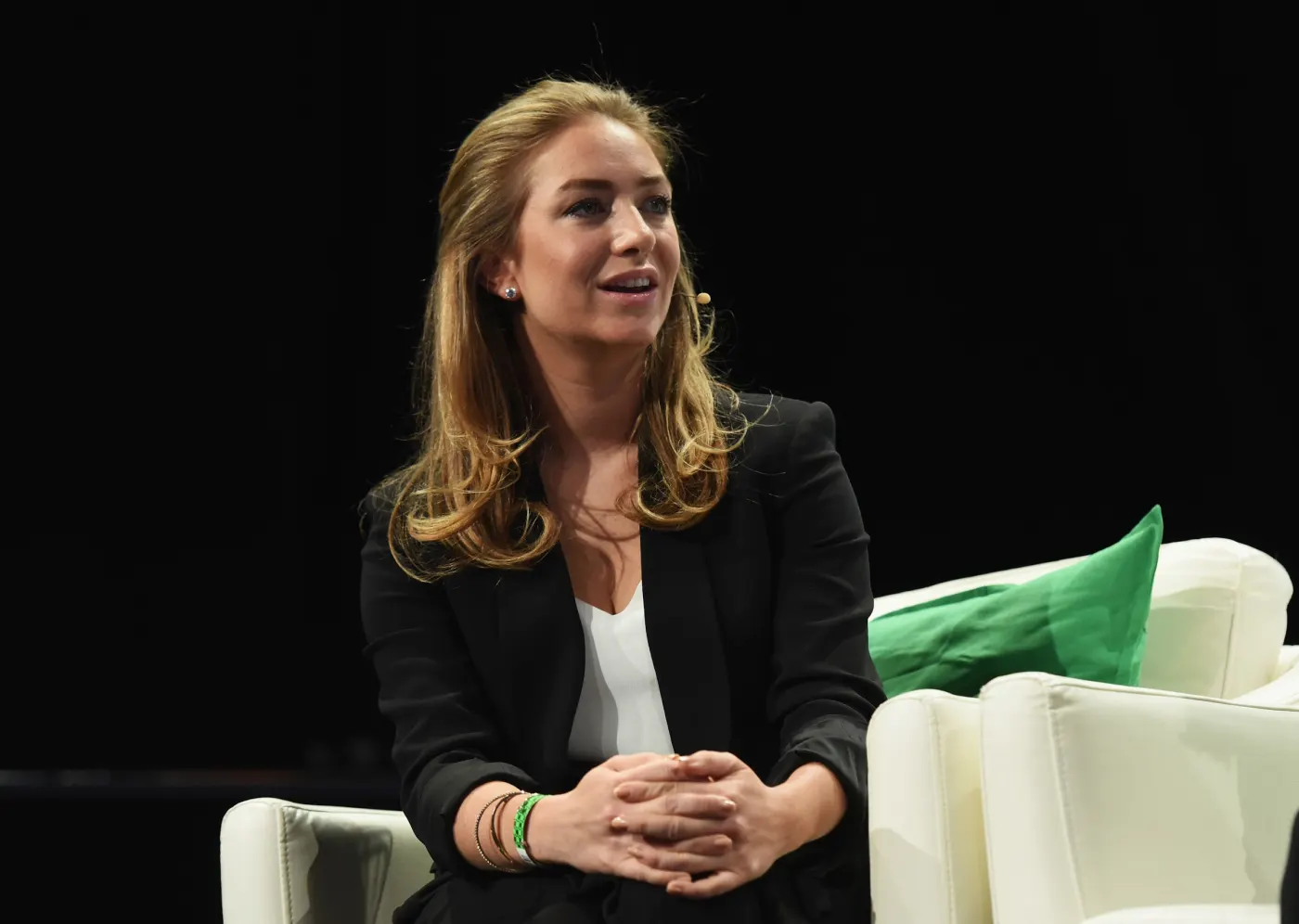 Wolfe Herd seated on stage in a black blazer, green pillow beside her